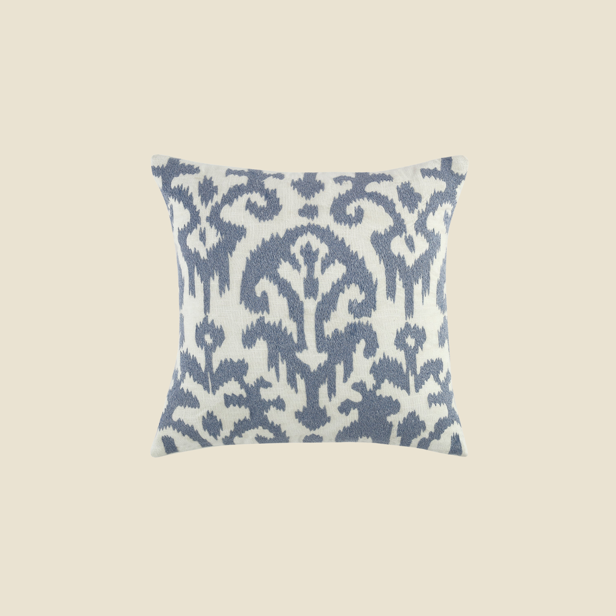 A square throw pillow featuring a blue ikat pattern on a white background, centered against a solid beige backdrop.