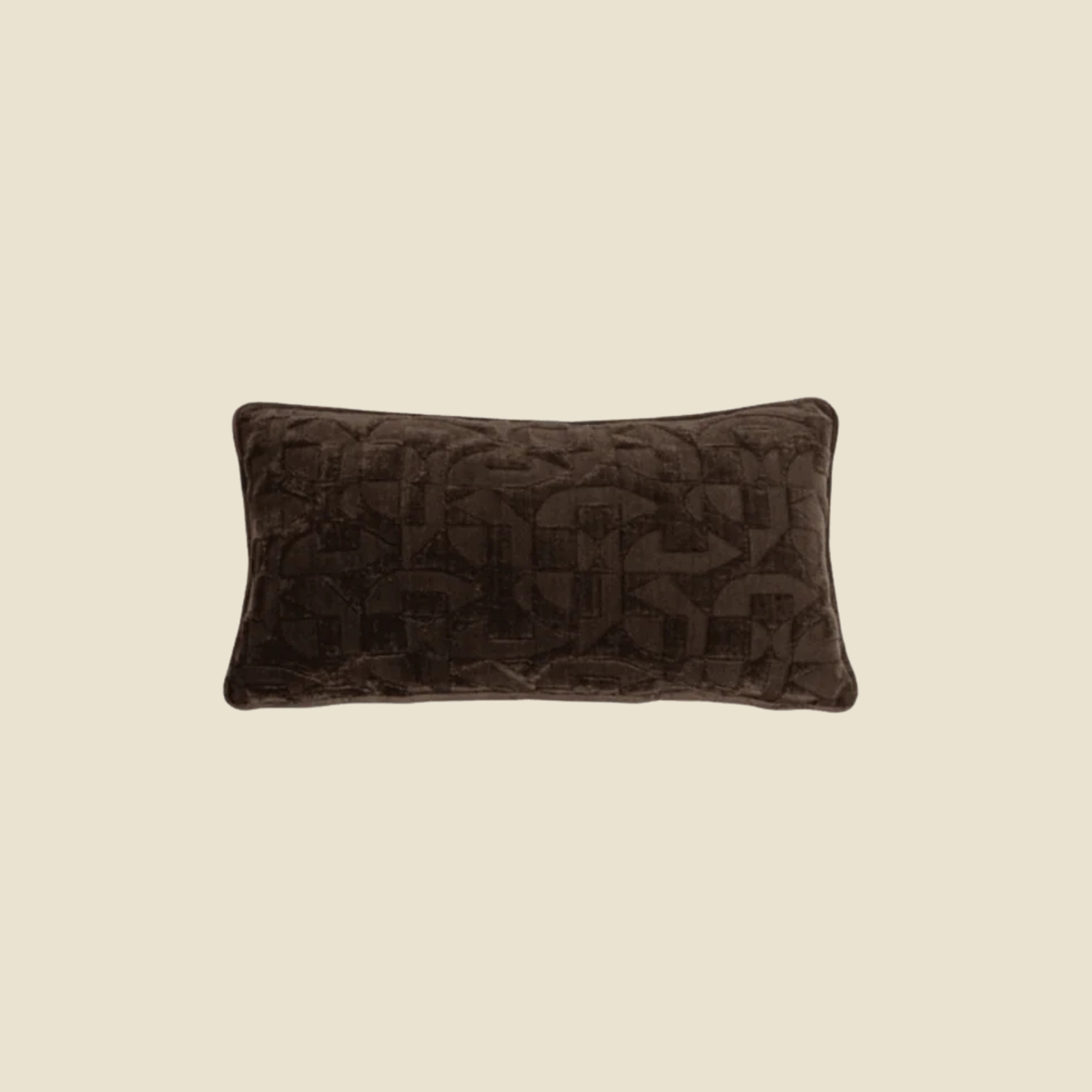 A rectangular lumbar pillow in dark brown velvet with an embossed geometric monogram pattern, centered on a solid beige background.