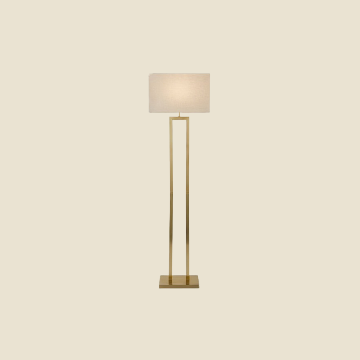 A modern floor lamp with a slim rectangular gold metal frame and a warm white fabric drum shade, centered against a solid cream background.
