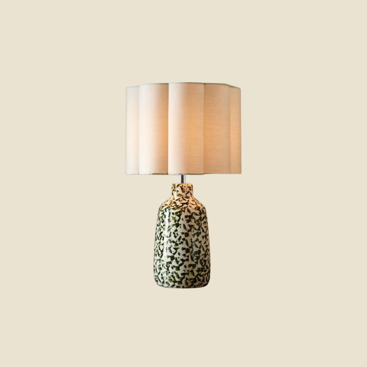 A table lamp with a beige pleated fabric drum shade and a glossy ceramic base featuring a black and white abstract pattern, shown against a solid light beige background.