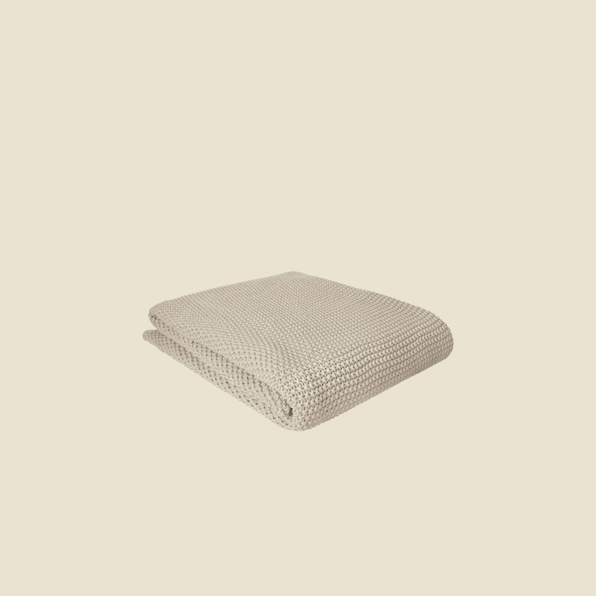 A folded knit blanket in a light oatmeal beige color, shown against a solid cream background.