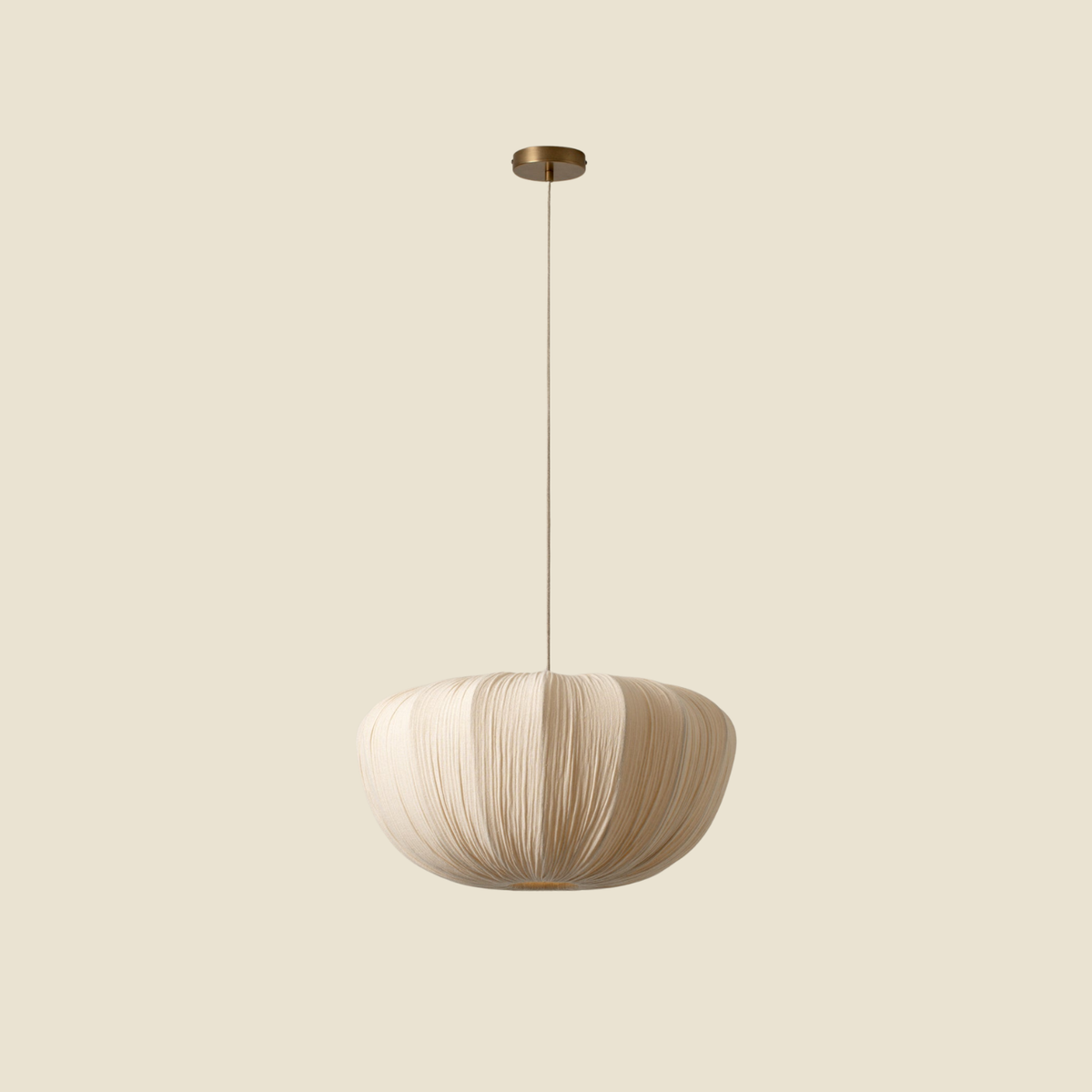 A modern pendant light with a textured, pleated beige shade and a brass ceiling canopy, suspended against a solid beige background.
