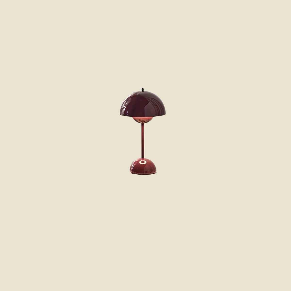 A small table lamp with a glossy dark red dome-shaped shade and matching stem and base, centered on a plain warm beige background.