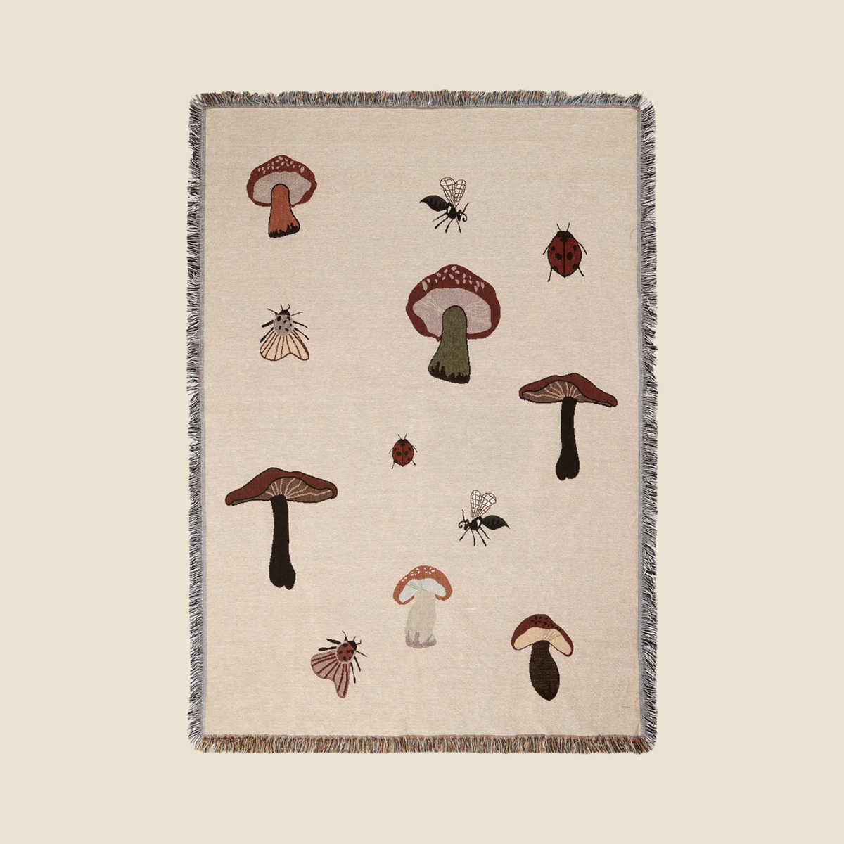 A square woven throw blanket with a natural beige linen-like background, featuring a pattern of embroidered mushrooms, beetles, and flies. The blanket has a gray and brown fringed border and is displayed flat against a solid beige background.