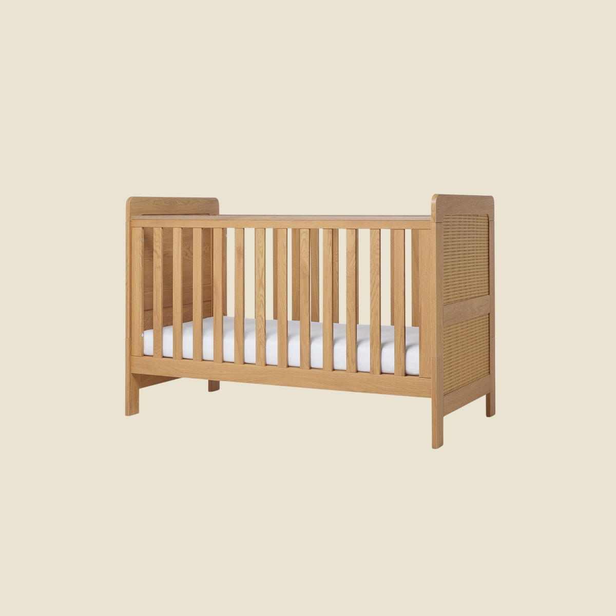 A light natural wood baby crib with a woven cane headboard panel and a white mattress, shown against a solid beige background.