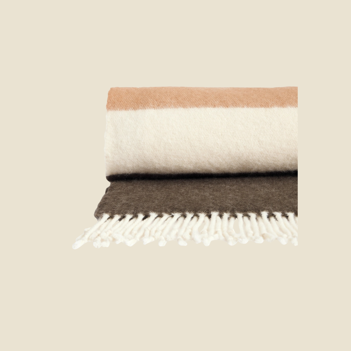 A folded woven throw blanket with white fringe, featuring horizontal stripes in warm tan, cream, and dark brown, set against a solid beige background.